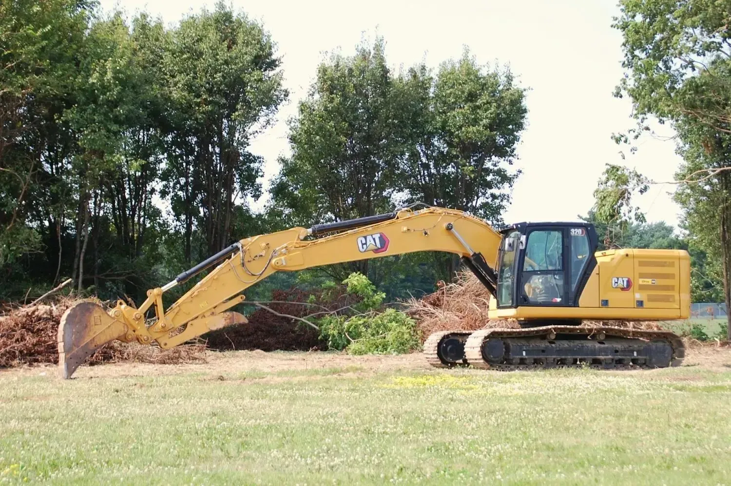 Excavator near trees and brush on a rural lot